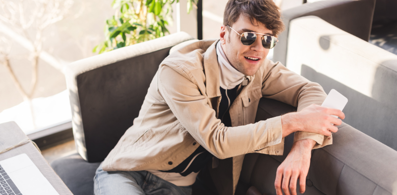 A man sat on a sofa wearing aviator sunglasses.
