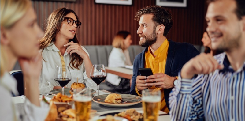 Multi-ethnic friends in a restaurant, chatting with a brunette woman wearing a pair of dark glasses.