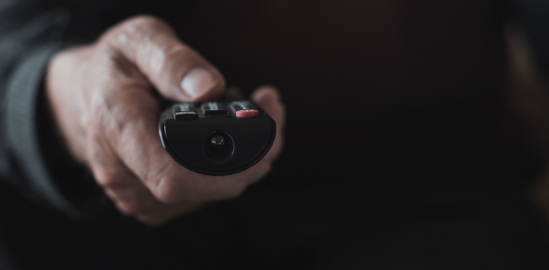 A close up of a senior man using a remote control to turn up the volume on the TV.
