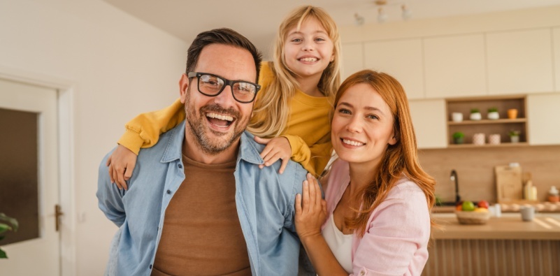 Parents experiencing a joyful moment in their home, father who is wearing glasses carrying daughter on his back.