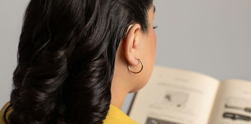 A girl reading a book, photo taken from the side to feature hearing aid