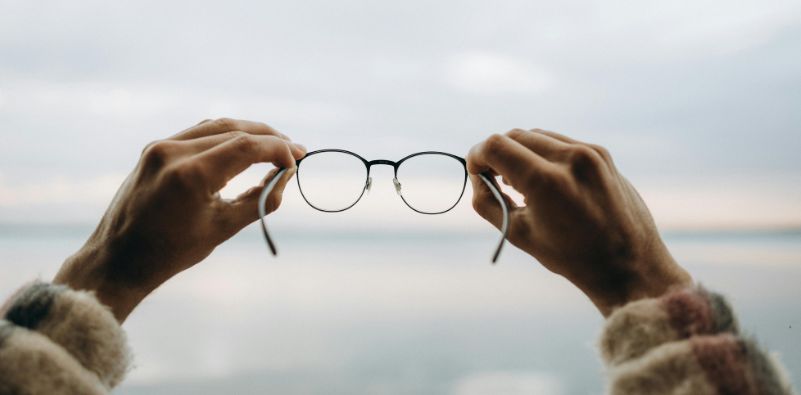 hands holding up a pair of optical glasses in a sky background